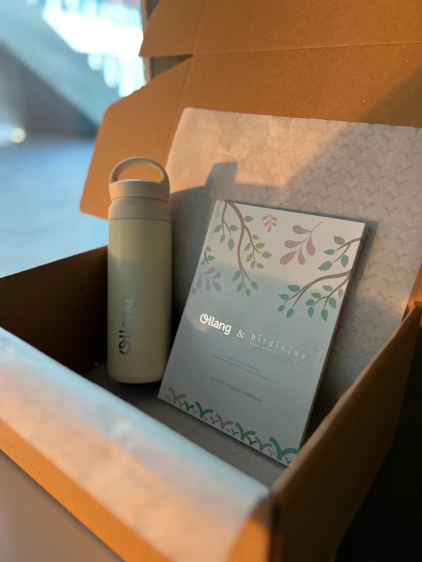 Çiçek desenli su şişesi ve defter bir kutunun içinde duruyor.